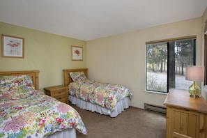 Une chambre avec deux lits, une table de chevet, une commode et une fenêtre donnant sur les arbres.
