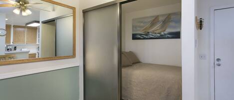 A bedroom with a sliding door, a bed, a painting of a sailboat, a ceiling fan, and a mirror.