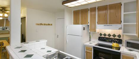 A kitchen with white tiles, wooden cabinets, a refrigerator, stove, microwave, and a sink.