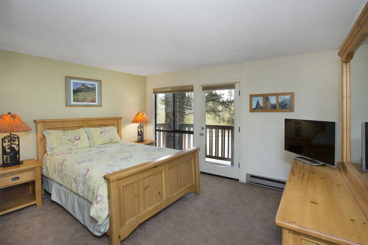 A bedroom with a wooden bed, two bedside lamps, a television, and a door leading to a balcony.