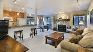 A spacious living area with a fireplace, wooden furniture, and a kitchen with modern appliances.