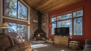 A cozy living room with a fireplace, leather sofas, and large windows offering a view of trees.