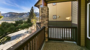 A balcony with a stone pillar, a wooden railing, and a view of a mountain range. - Eagle Run by 101 Great Escapes (Mammoth Lakes)