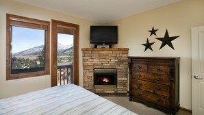 A bedroom with a stone fireplace, a bed with a striped bedspread, a dresser, and a TV mounted above the fireplace. - Eagle Run by 101 Great Escapes (Mammoth Lakes)