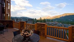 A balcony with a stone railing, a round table with chairs, and a vase of flowers. - Sunstone Lodge by 101 Great Escapes (Mammoth Lakes)