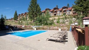 A pool area with lounge chairs, a clear blue pool, and a hillside with multi-story buildings in the background. - Sunstone Lodge by 101 Great Escapes (Mammoth Lakes)