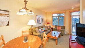A cozy living room with a wooden dining table, a sofa, a coffee table, and a TV. - Sunstone Lodge by 101 Great Escapes (Mammoth Lakes)