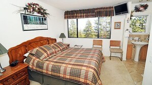 A bedroom with a large bed, a desk, a chair, a TV, and a window with a view of trees. - Mammoth Point by 101 Great Escapes (Mammoth Lakes)