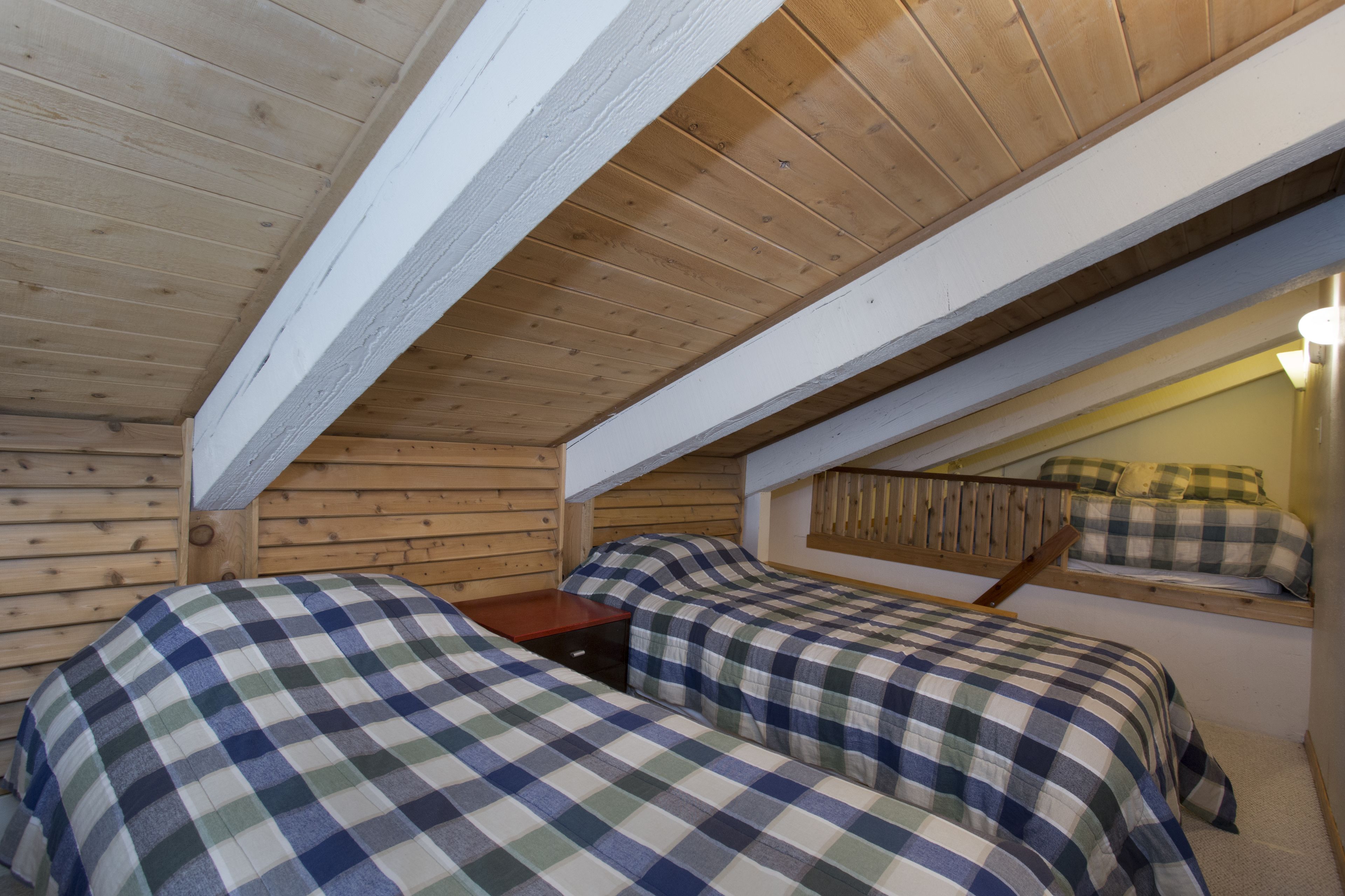 A bedroom with two beds, wooden walls, and a sloped ceiling.
