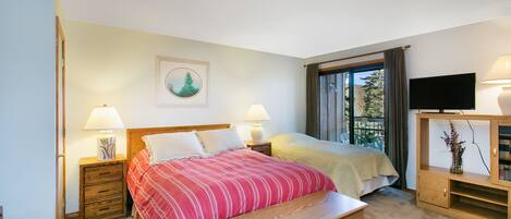 A bedroom with two beds, a wooden bench, a TV, and a window with curtains.