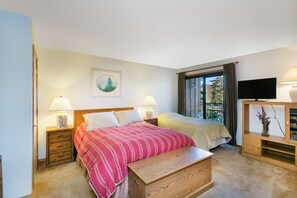 Een slaapkamer met twee bedden, een houten bankje, een televisie en een raam met gordijnen.