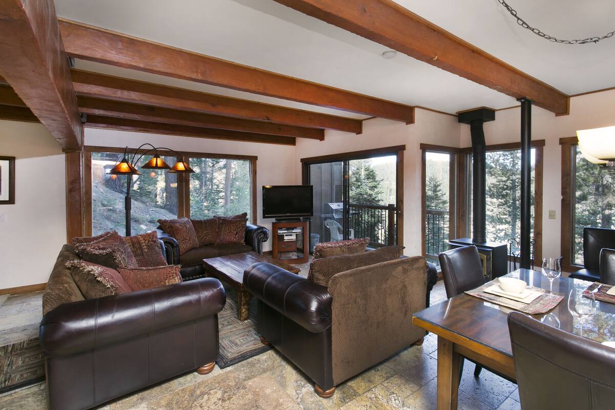 A cozy living room with a fireplace, leather sofas, a dining table, and large windows offering a view of the outdoors.