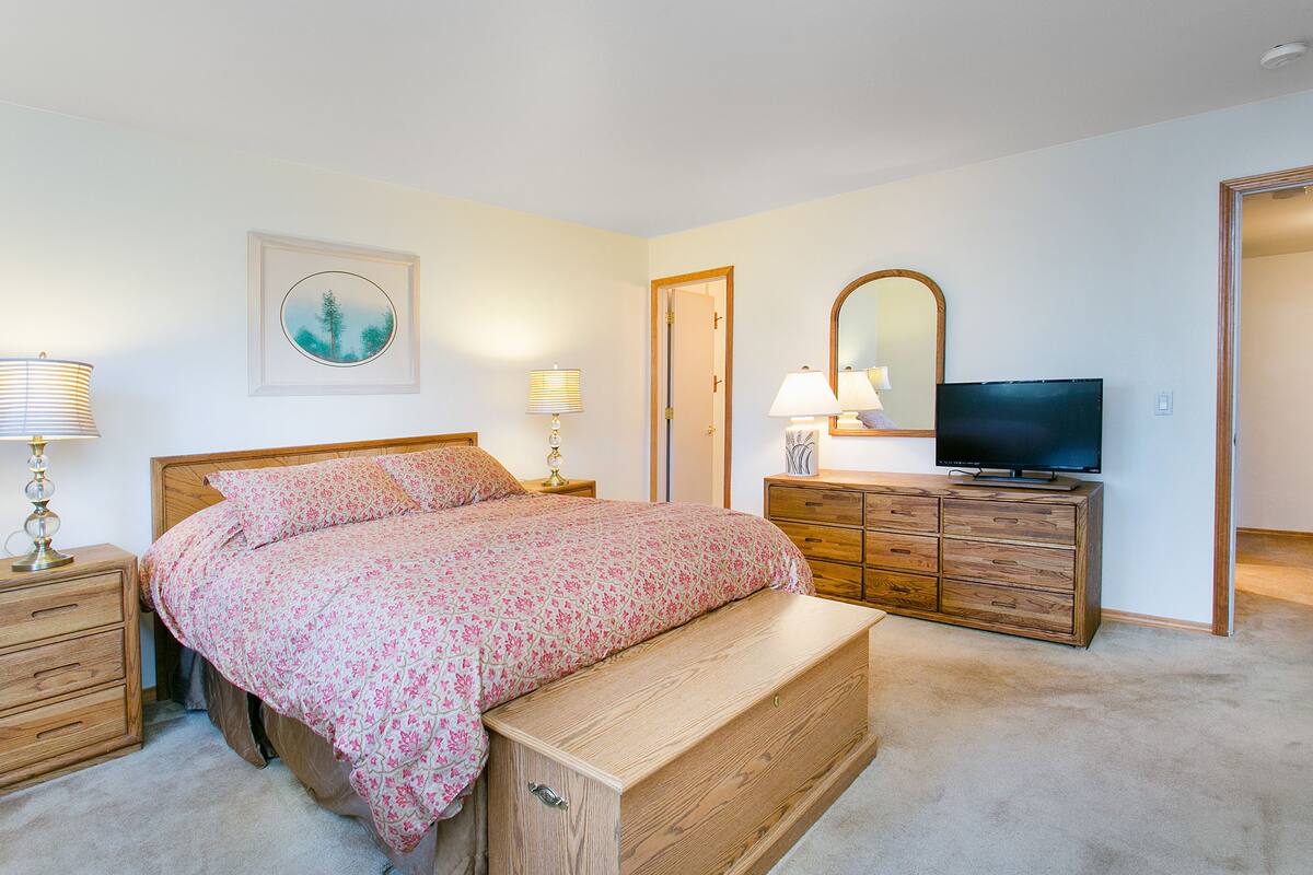 A bedroom with a bed, bedside tables, a dresser, a television, and a mirror.