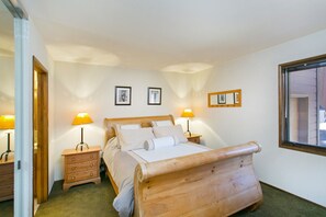 Un dormitorio con una cama de madera, dos mesitas de noche con lámparas, un espejo y cuadros en la pared.