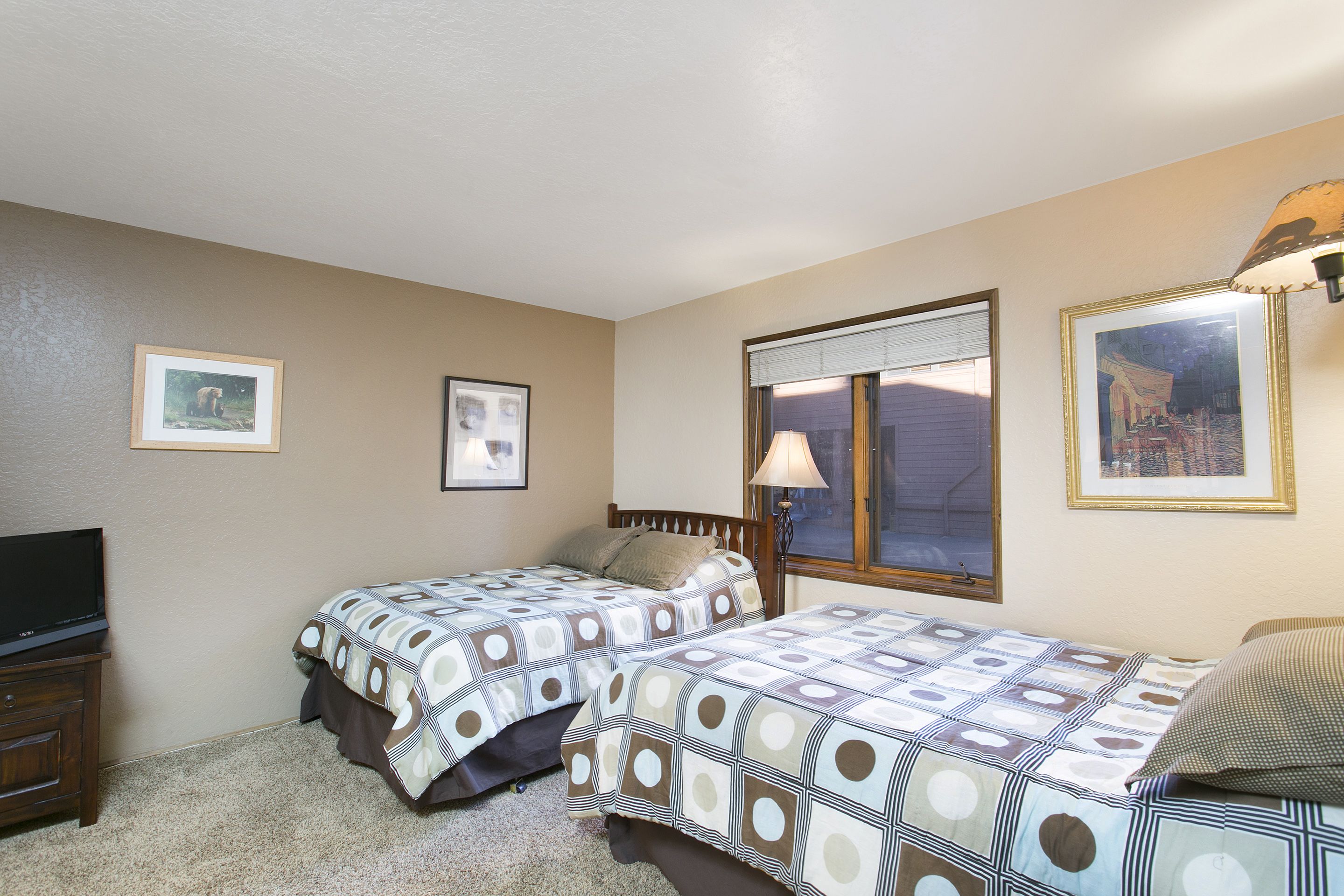 A bedroom with two beds, a TV, and framed pictures on the wall.