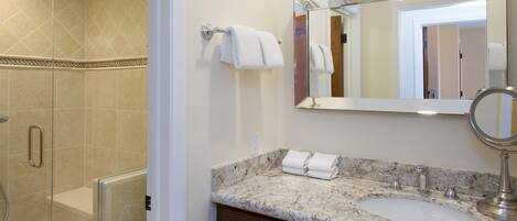 A bathroom with a marble sink, a large mirror, and a glass shower enclosure.