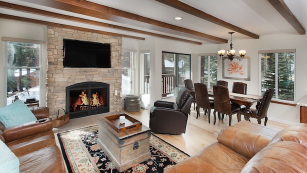 Un salón espacioso con chimenea de piedra, muebles de cuero y grandes ventanales que ofrecen vistas al exterior.