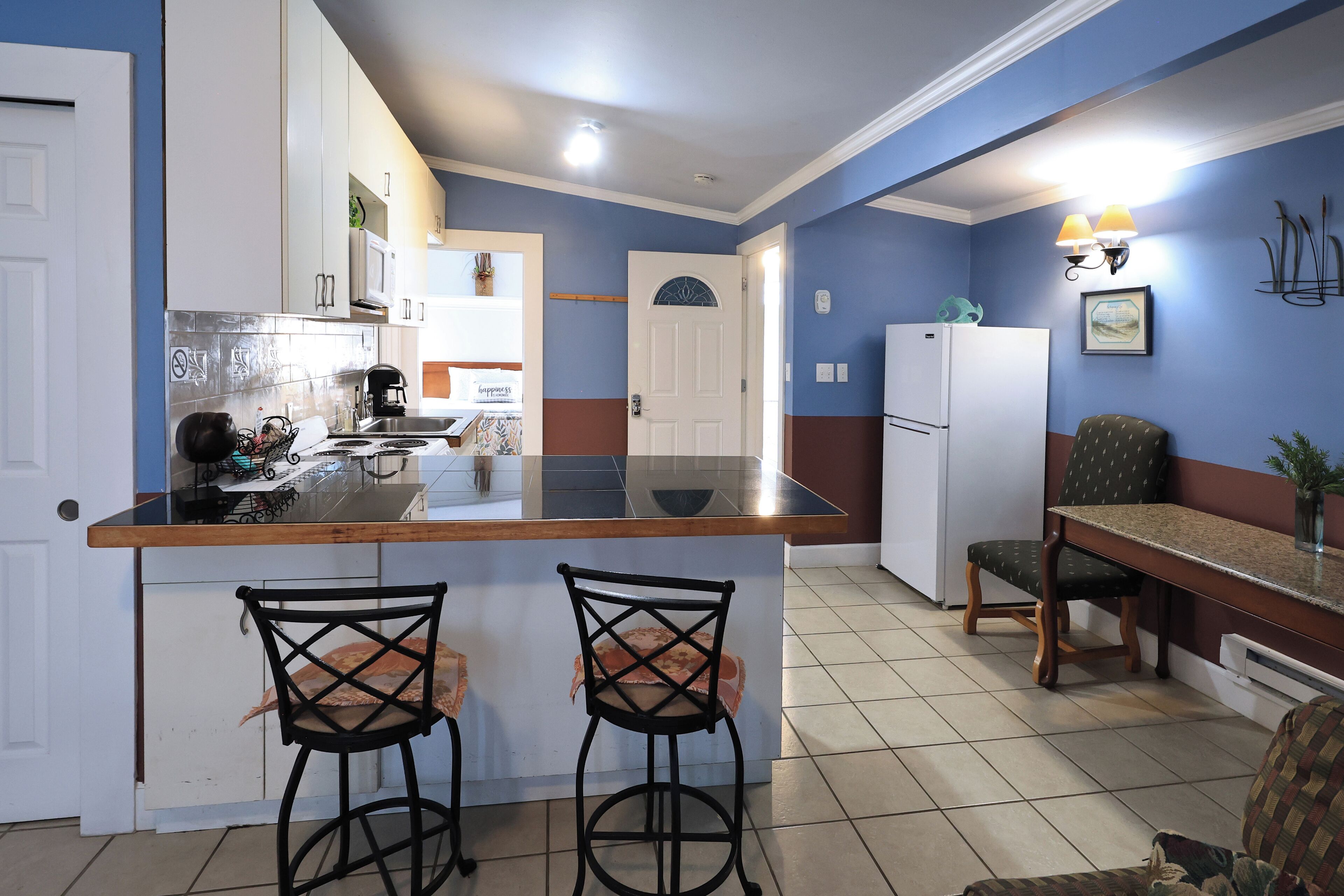 A kitchen with a central island, two bar stools, a dining table with chairs, and a refrigerator.