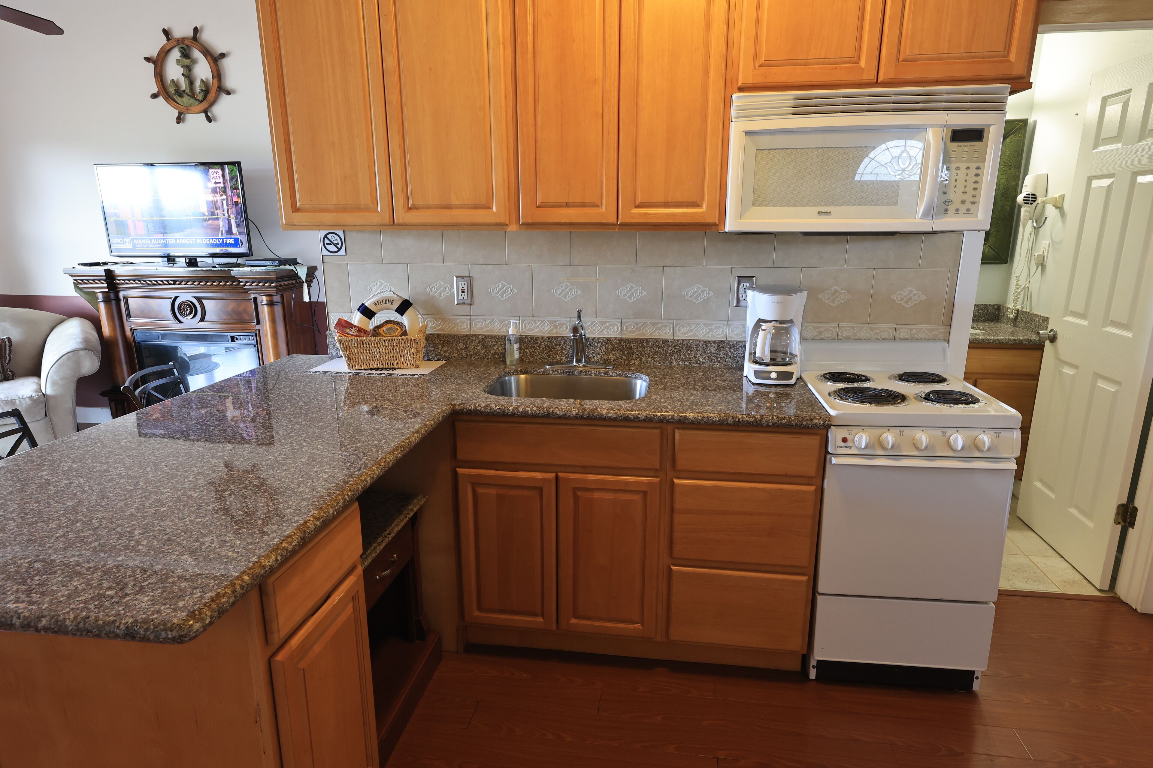A kitchen with wooden cabinets, a granite countertop, a microwave, a stove, and a sink.