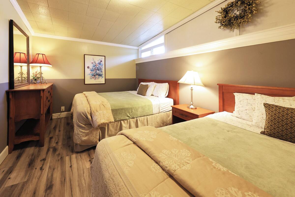 A hotel room with two beds, a wooden dresser, a mirror, and a window.