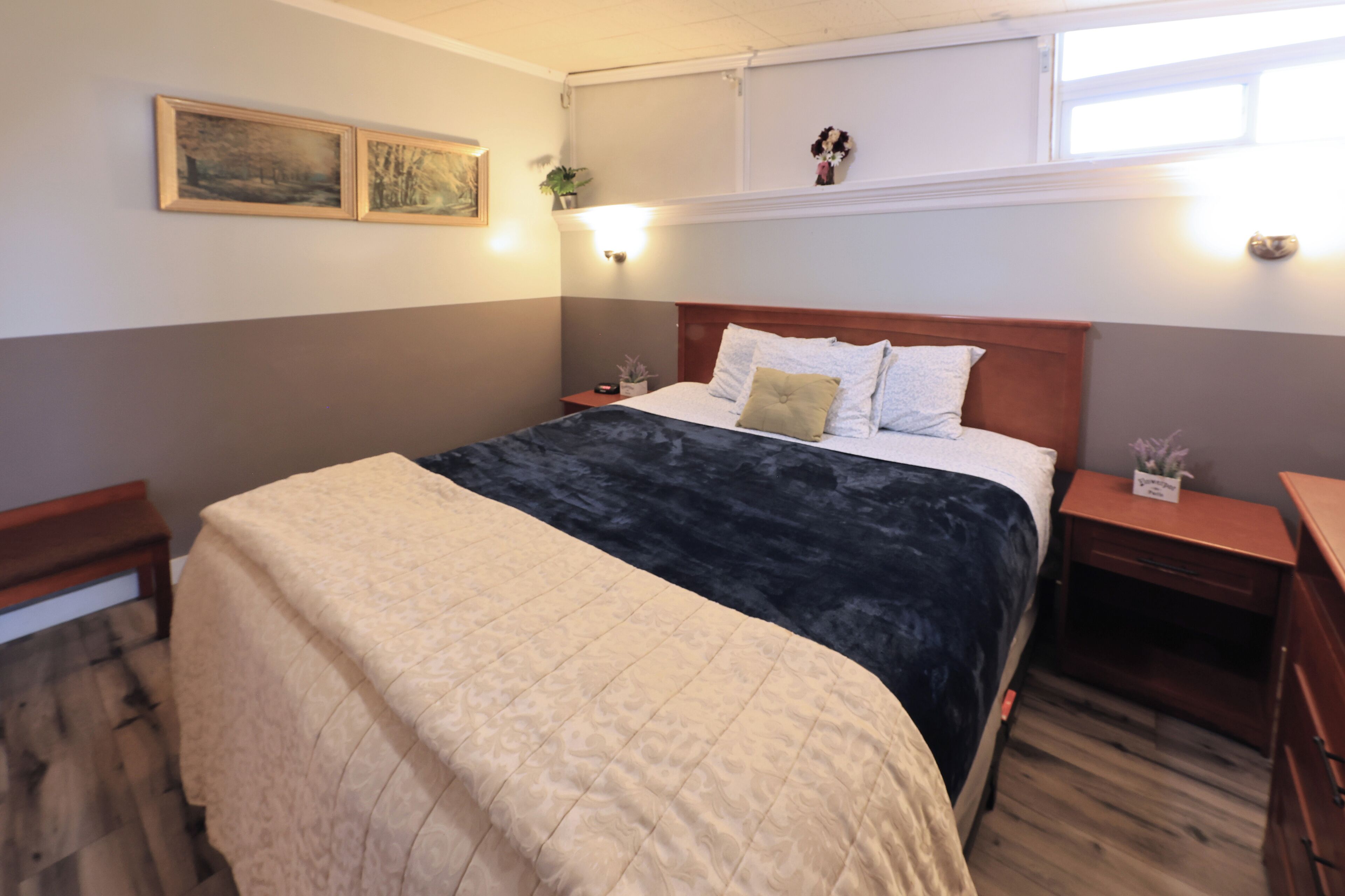 Une chambre à coucher comprenant un lit, des tables de chevet, une commode, un banc et des œuvres d’art accrochées au mur.