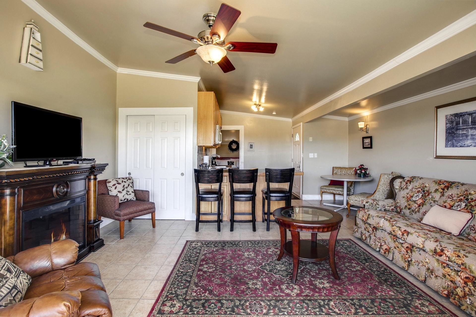 A living room with a fireplace, leather sofa, a TV, a ceiling fan, and a floral sofa.