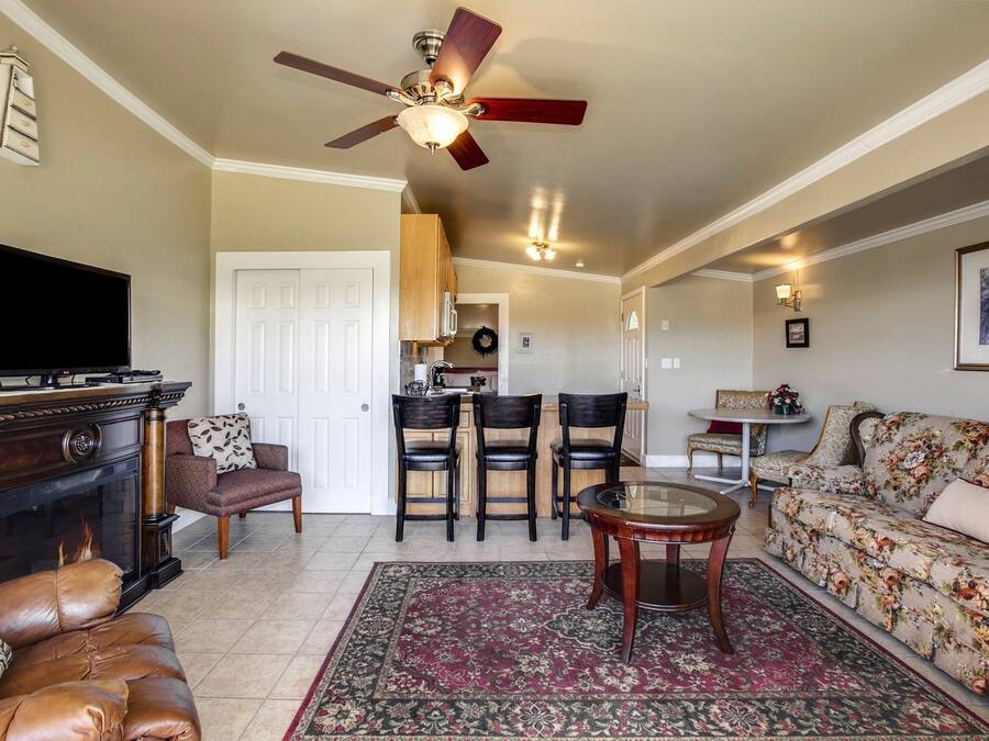 A living room with a fireplace, leather sofa, a TV, a ceiling fan, and a floral sofa.