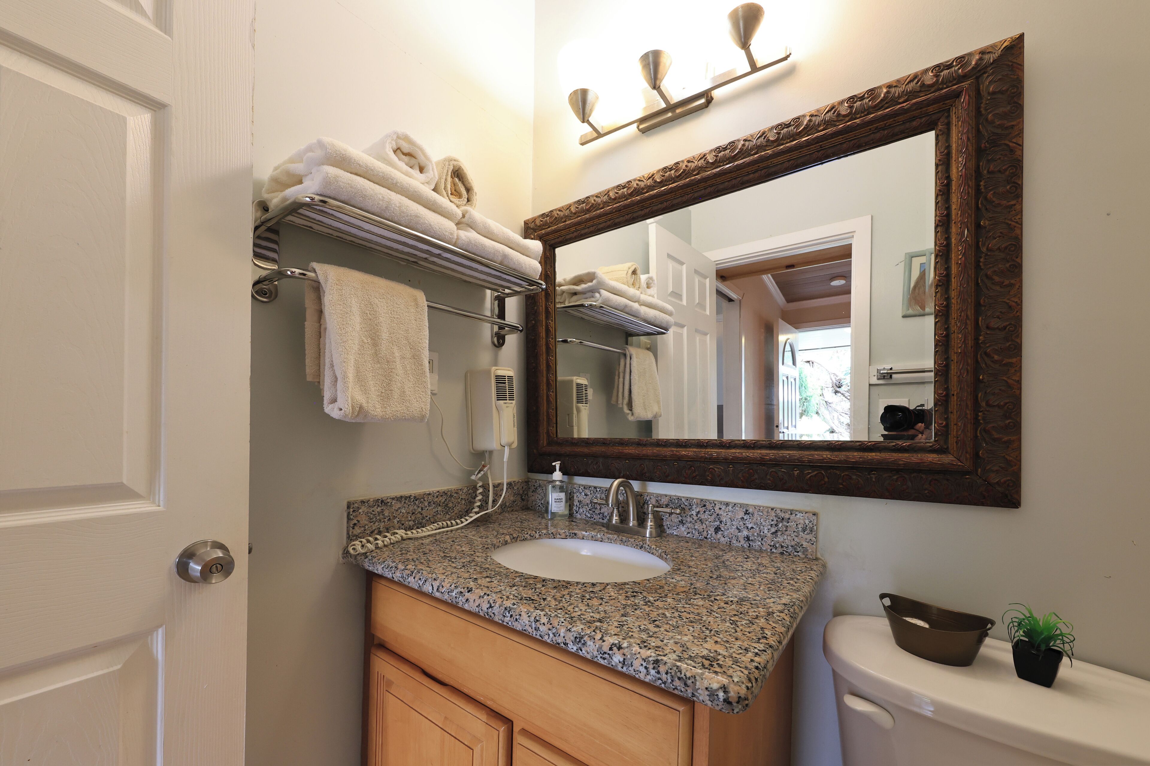 Une salle de bain avec un lavabo doté d’un plan de travail en granit, un meuble-lavabo en bois, un grand miroir et un porte-serviettes avec des serviettes pliées.