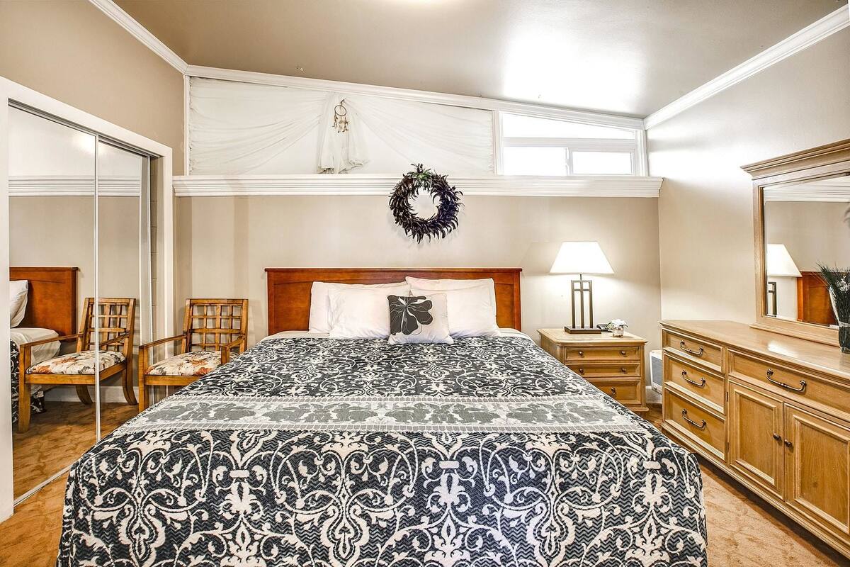 A bedroom with a large bed, a wooden nightstand, a dresser, and a mirror.
