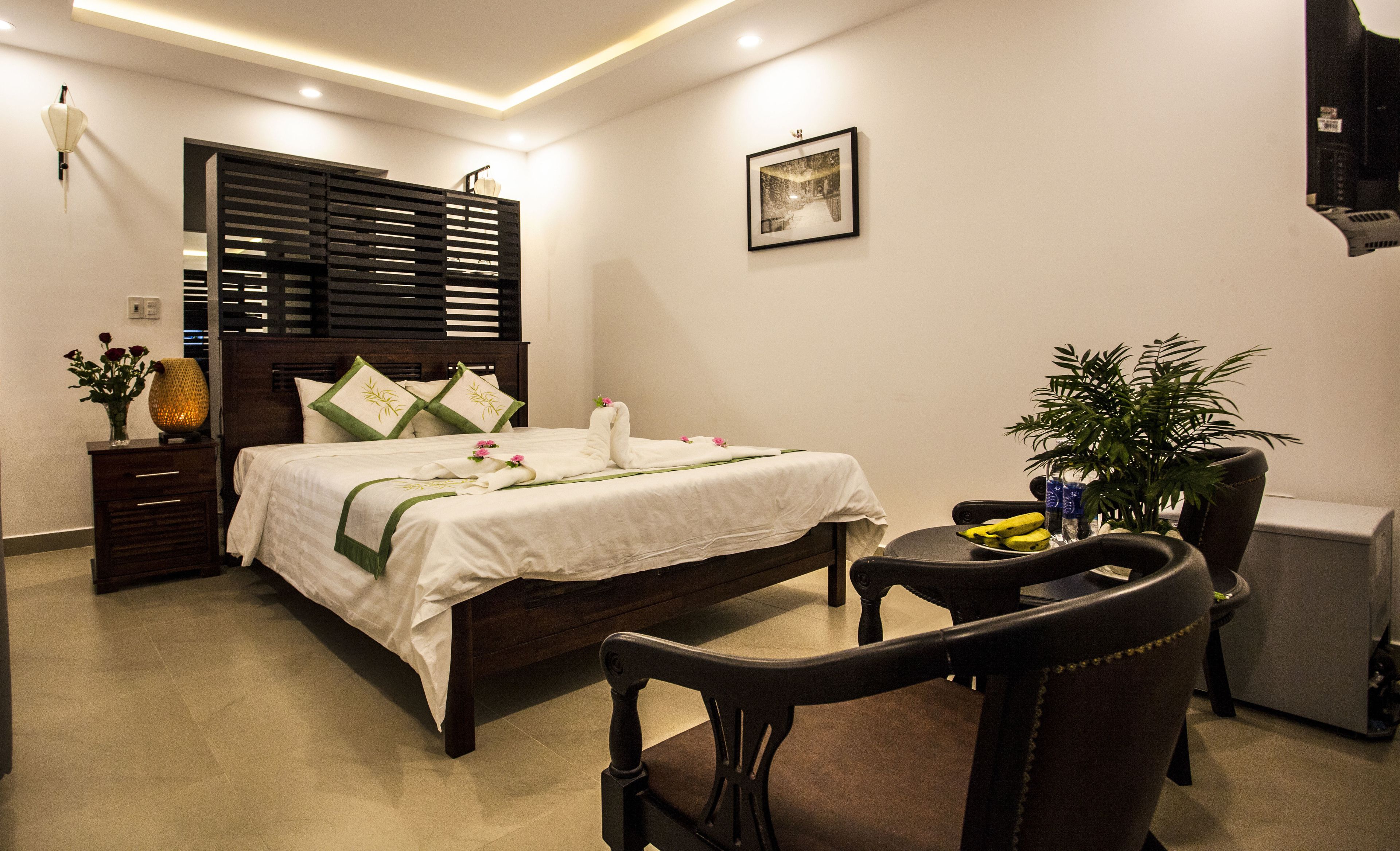 A neatly arranged hotel room with a bed, bedside table, chair, and a small table with a plant.