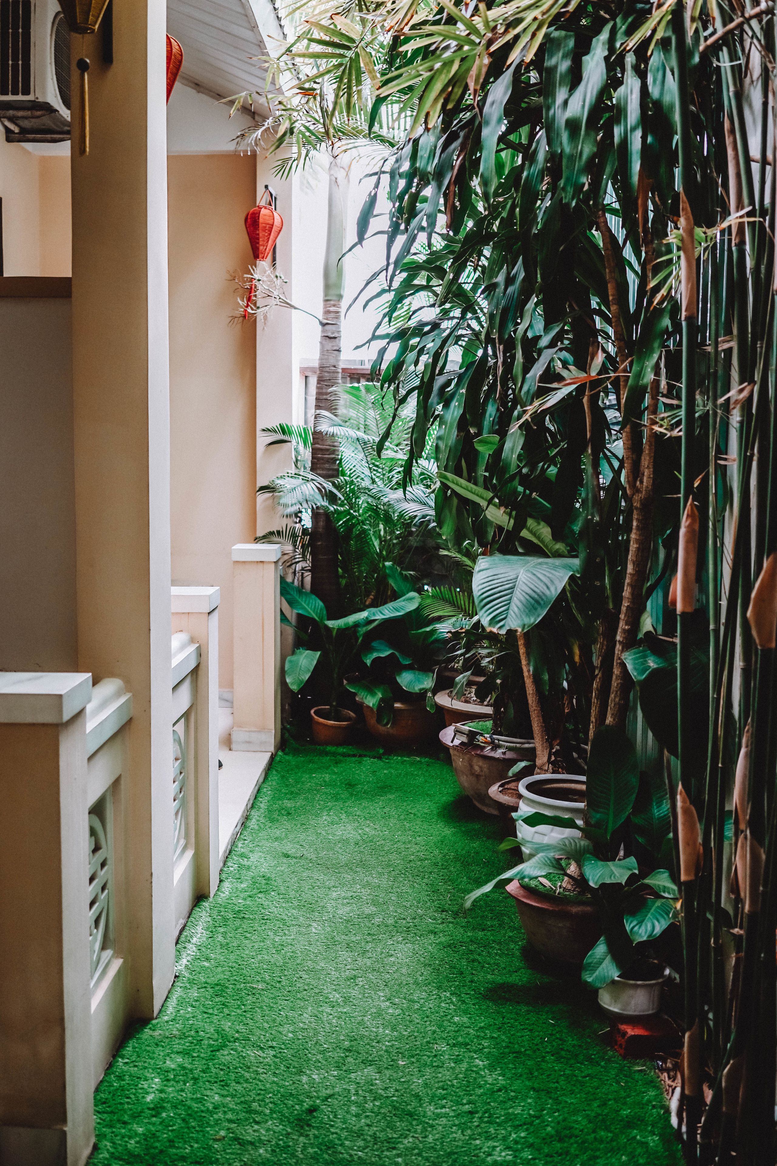 Corredor estreito com grama sintética verde, plantas em vasos e um corrimão branco.
