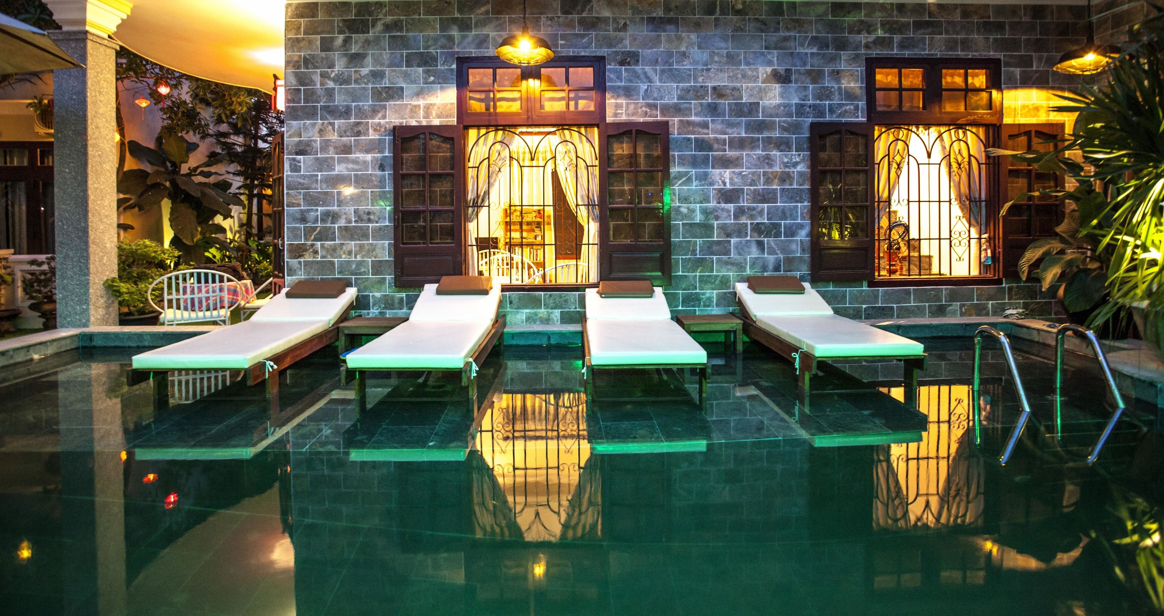 A pool area with lounge chairs and a stone wall with windows.