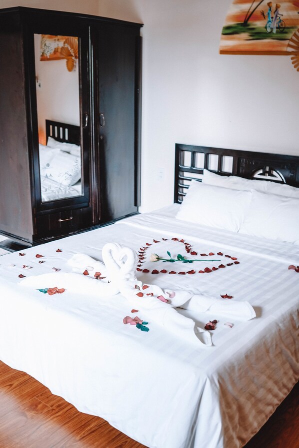 A neatly made bed with a heart-shaped arrangement of rose petals and a white towel.