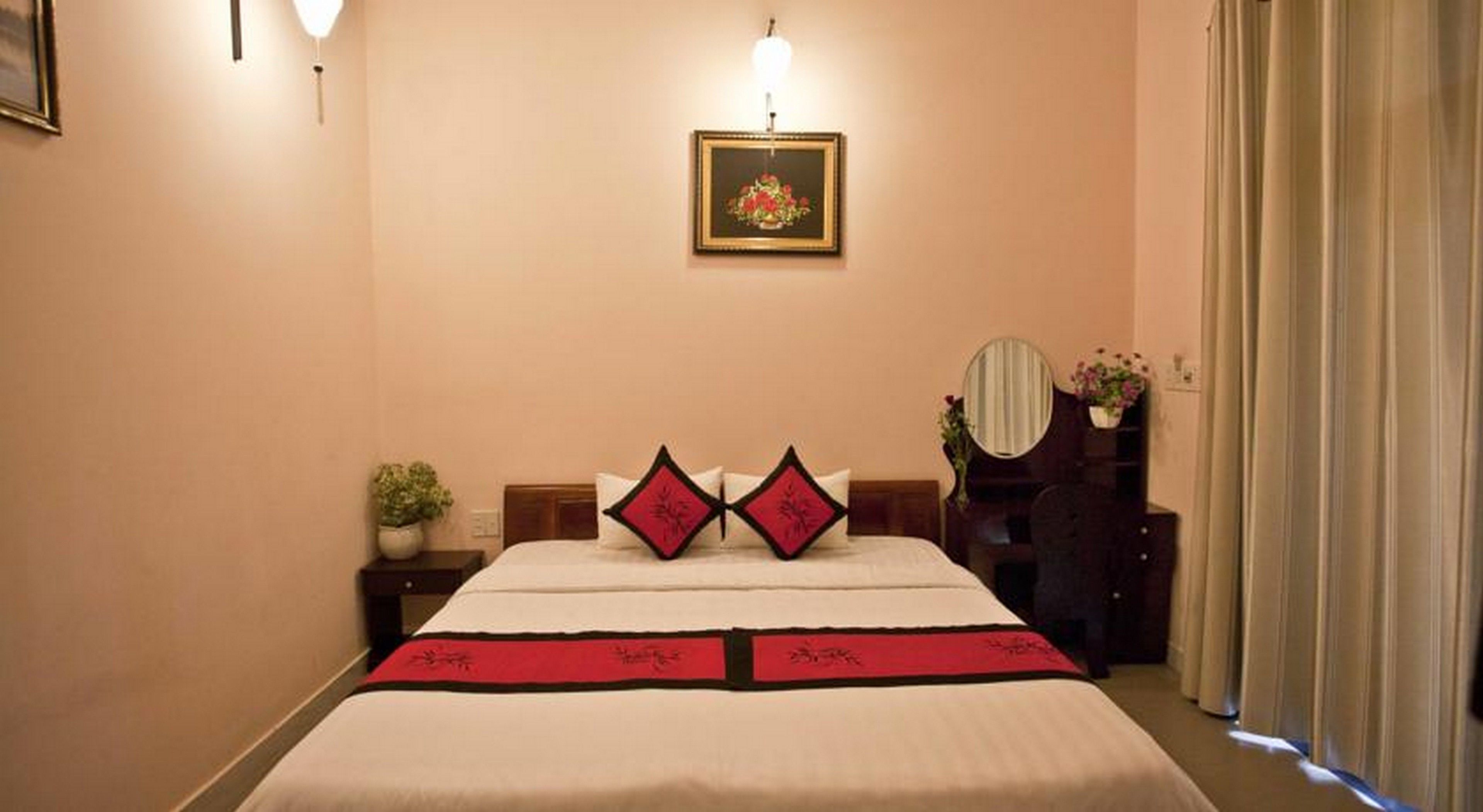 A hotel room with a large bed, a bedside table with a plant, a dresser with a mirror, and a framed picture on the wall.