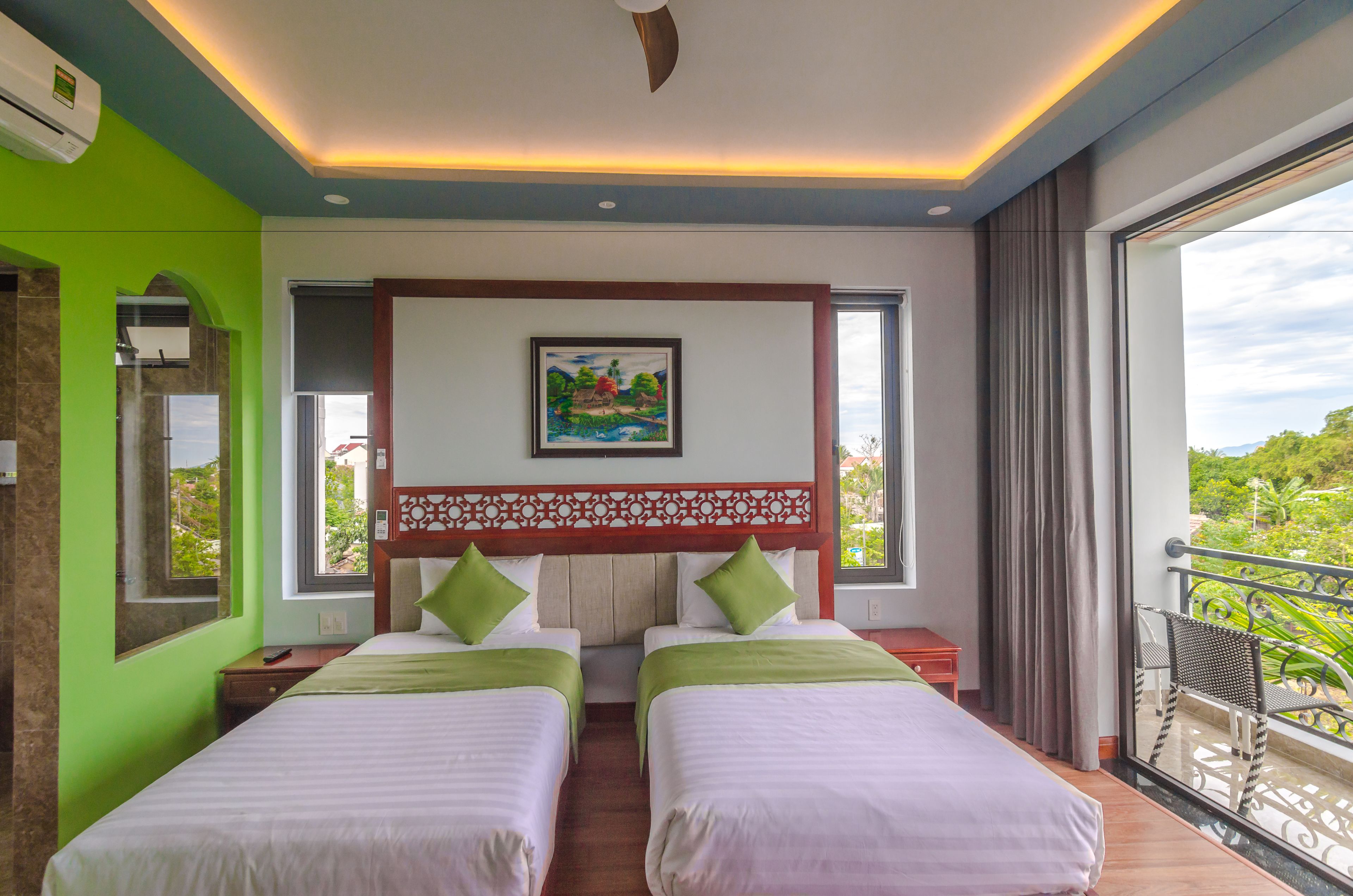 A hotel room with two beds, a large window with a view, a ceiling fan, and a painting on the wall.