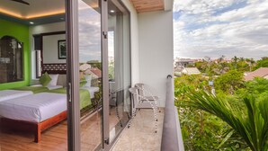 Ein Schlafzimmer mit einem Bett, einer Glastür, die auf einen Balkon mit einem Sessel führt, und Blick auf die Umgebung.