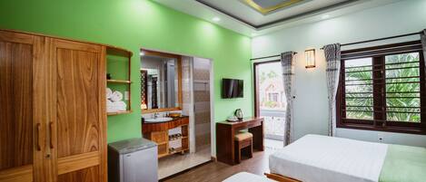 A hotel room with a green wall, wooden wardrobe, a small desk, a bed, and a window with curtains.