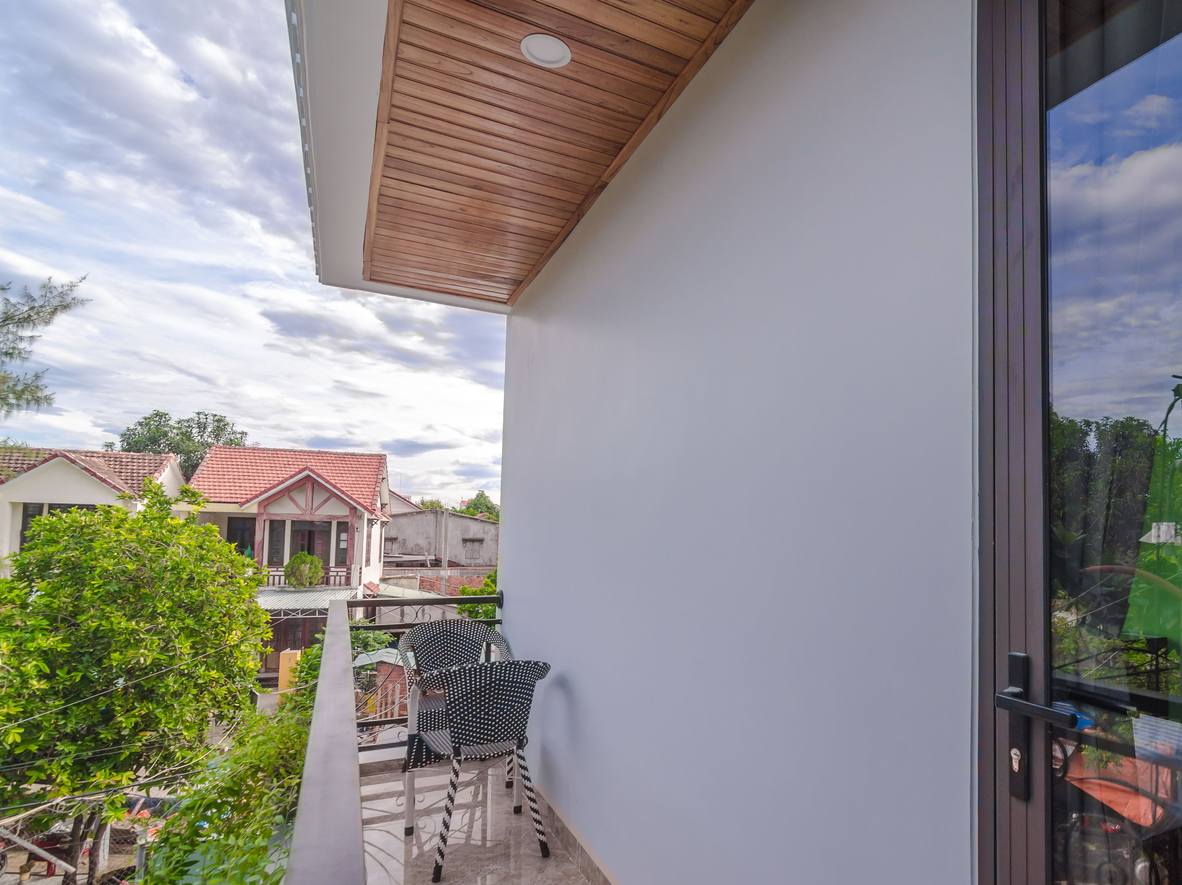 Un balcón con techo de madera, una silla y vista a casas vecinas.