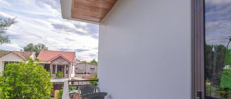 Un balcón con techo de madera, una silla y vista a casas vecinas.