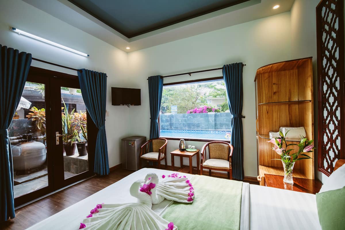 A hotel room with a bed, a desk, two chairs, a TV, and a view of the outside.