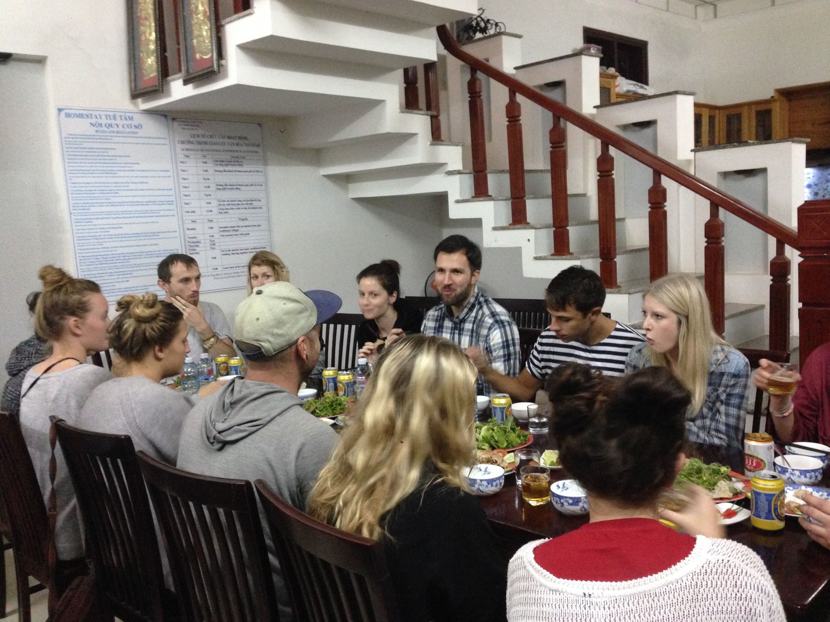 Un groupe de personnes est assis autour d’une table dans un espace dédié à la restauration, avec un escalier en arrière-plan.