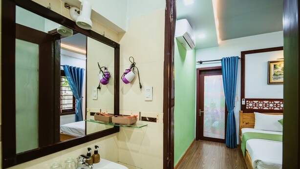 A hotel room with a large mirror, a sink, a bed, and a door with a curtain. - Tue Tam Villa (Da Nang)