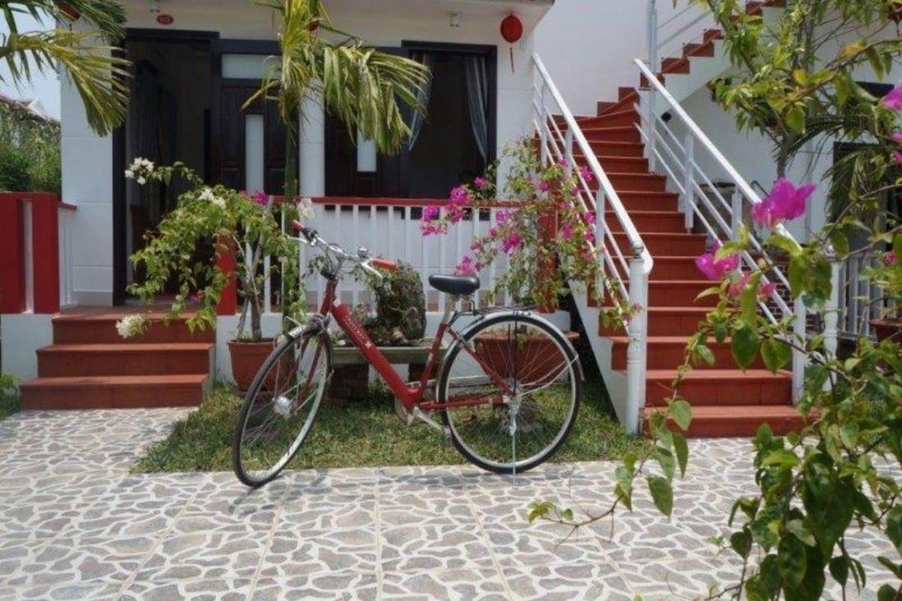 Una bicicleta aparcada en un porxo empedrat amb una escala que porta a una porta blanca.