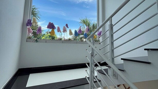 Una scala con ringhiera in metallo e una finestra che si affaccia su un giardino con fiori colorati.