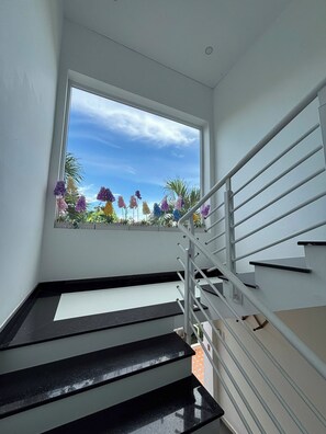 A staircase with a metal railing and a window overlooking a garden with colorful flowers. - Red House Homestay (Da Nang)