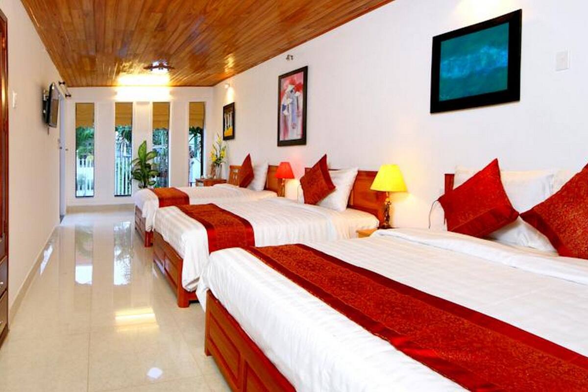 A hotel room with three beds, each with red and white bedding, and a wooden ceiling.