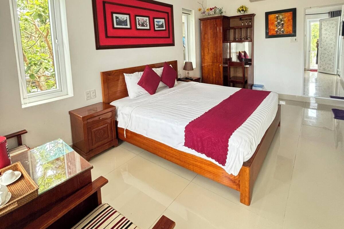 A spacious bedroom with a large bed, a wooden nightstand, a desk, and a bench.