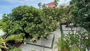 Un cortile con vegetazione lussureggiante, pavimento in piastrelle e un edificio con tetto rosso sullo sfondo.