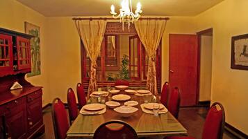 A dining room with a glass table set for eight, surrounded by red chairs.