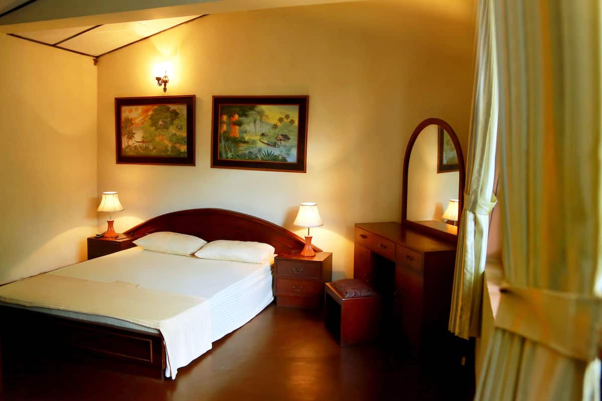 A neatly made bed with a white comforter and pillows, flanked by two bedside tables with lamps, a wooden nightstand, and a dresser with a mirror.